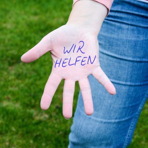 "Wir helfen" mit einem Stift auf der Innenfläche einer Hand geschrieben
