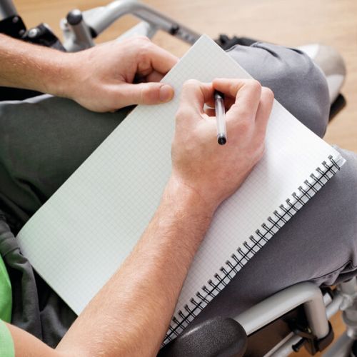 eine im Rollstuhl sitzende Person fertigt Notizen an