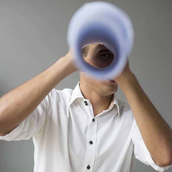 ein Mann schaut durch eine Zeitung, die zusammengerollt ein Fernrohr formt