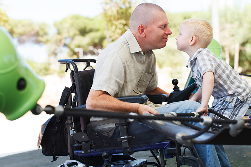 Vater im Rollstuhl neigt sich liebevoll zu seinem Sohn